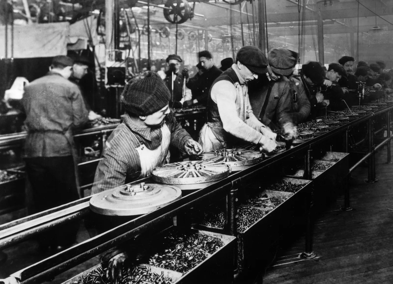 Workers along a moving assembly line at Ford's Highland Park plant in 1913, flywheel magnetos passing from one station to the next