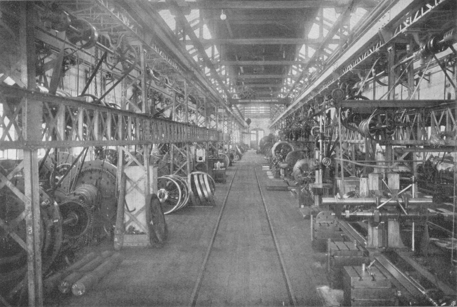 A long factory hall in 1910, with belts running down from overhead line shafts to every machine along both sides of a central aisle