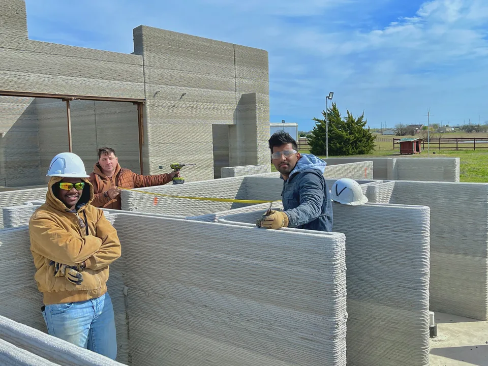 Three of the team on site, measuring across the printed walls with a tape.
